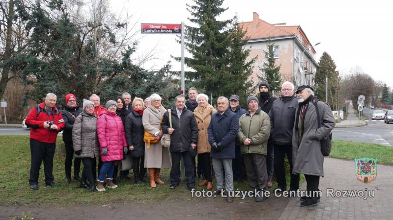 Grupa kilkunastu osób stojących przy odsłoniętej tabliczce z nazwą skweru